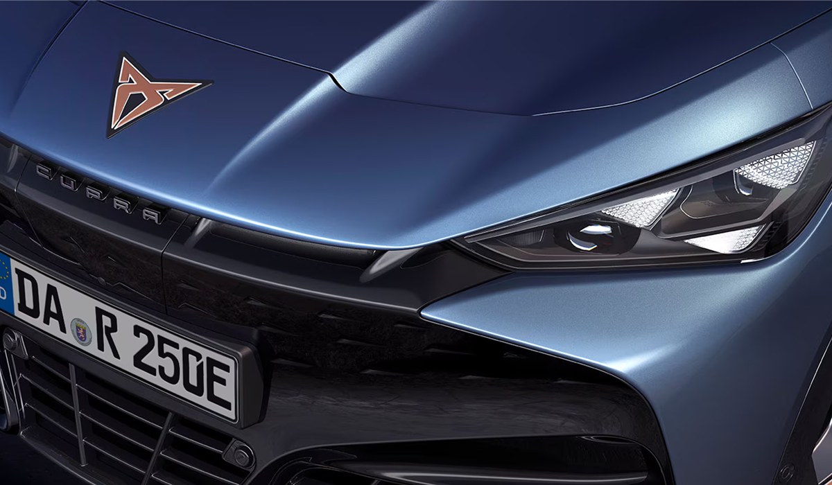 CUPRA Tavascan von hinten in einer Garage beim Laden an einer CUPRA Wallbox, violette Beleuchtung durch Fenster mit Berglandschaft.